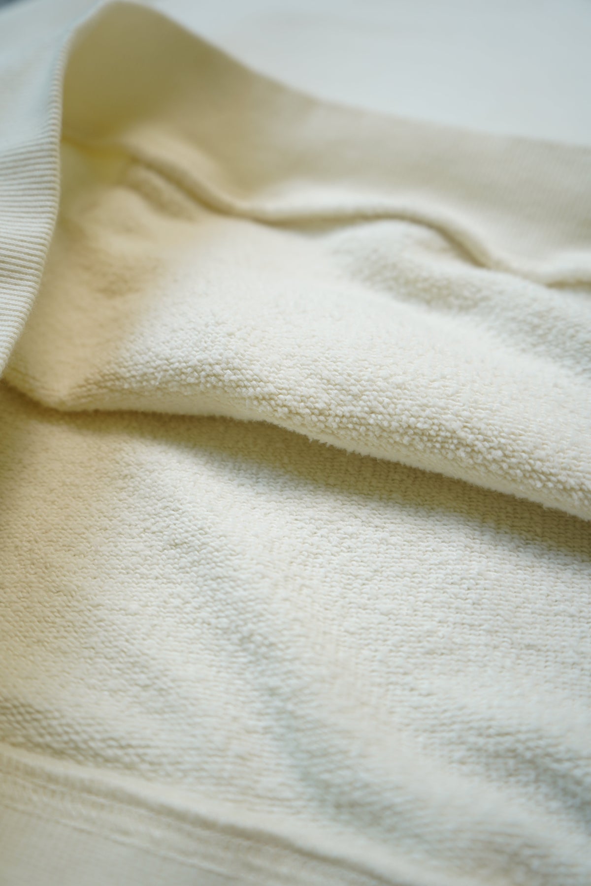 A close-up of a soft cream-colored knit fabric, showing the texture of the knit material and a ribbed collar.