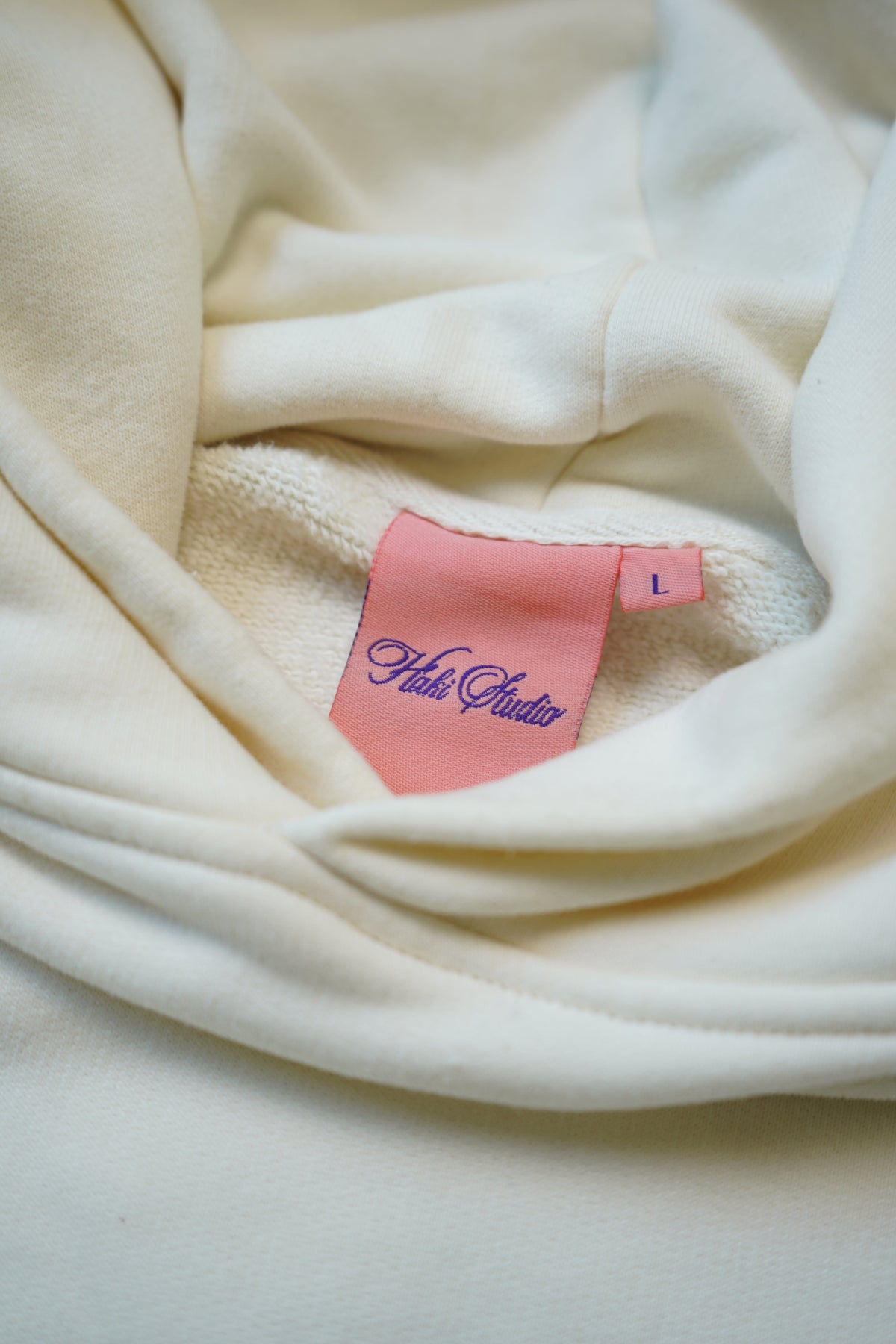 Close-up of a cream-colored fabric garment with a pink sewn-in size tag reading 'Halo Studio' and size 'L'.