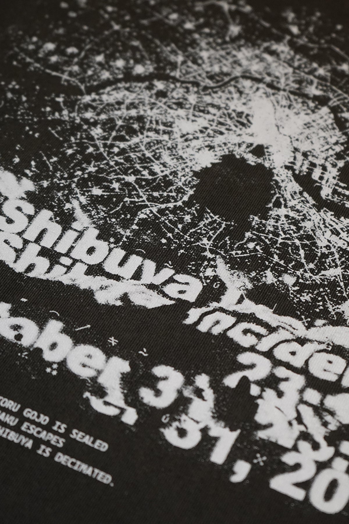 Close-up of the black Shibuya Incident Tee showing a distressed white printed map-like graphic with a dark blotch, and partly legible printed text