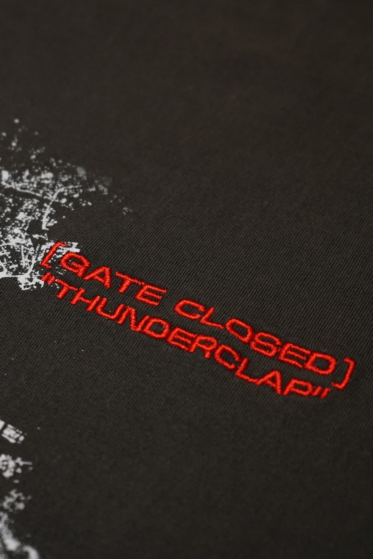 Close-up of the dark charcoal Shibuya Incident Tee showing red embroidered text reading [GATE CLOSED] "THUNDERCLAP" beside a distressed white graphic