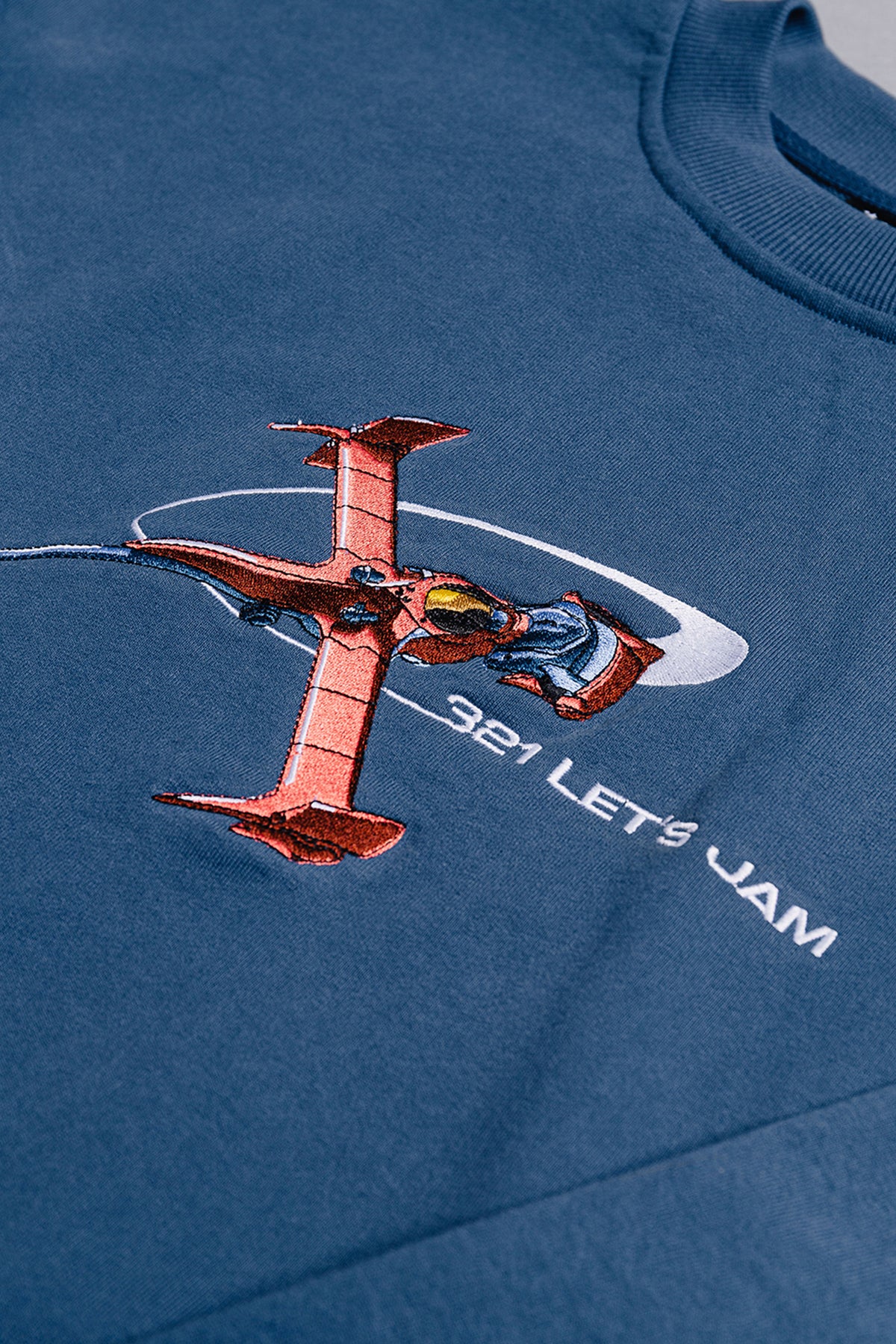 Close-up of the blue Let's Jam Crewneck front with embroidered red fighter ship in a white swoosh and white text reading 321 LET'S JAM