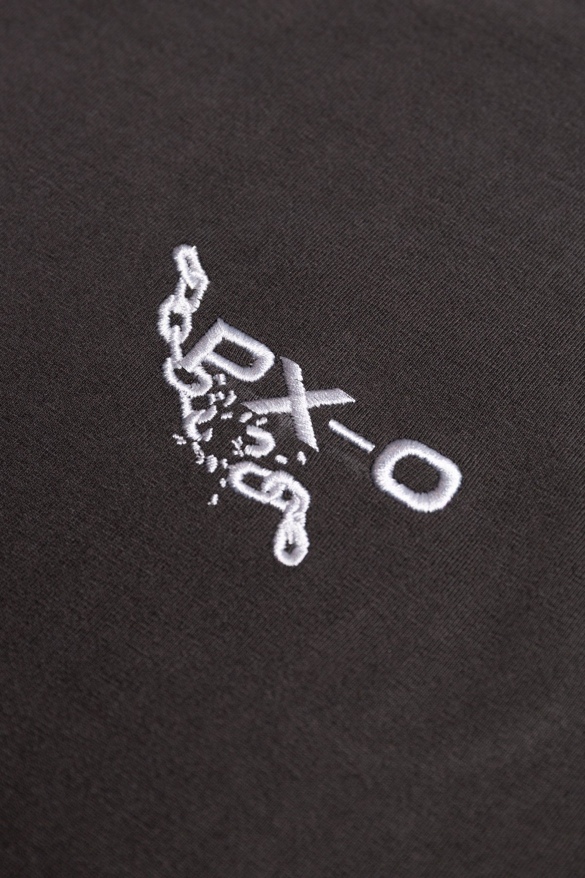 Close-up of a black fabric surface with a small white embroidered logo reading PXO.