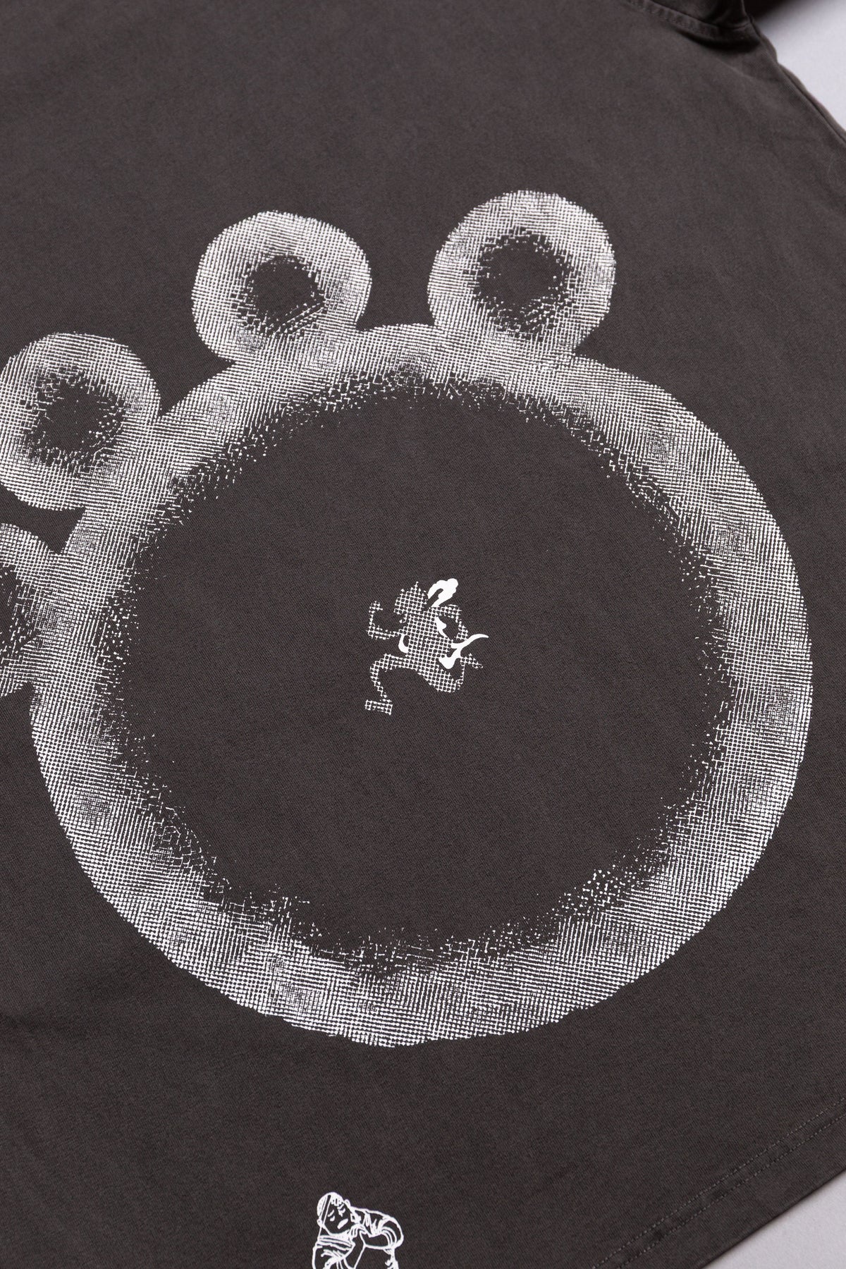 A close-up of a dark charcoal gray t-shirt featuring a large white textured circular graphic with three circular elements at the top.