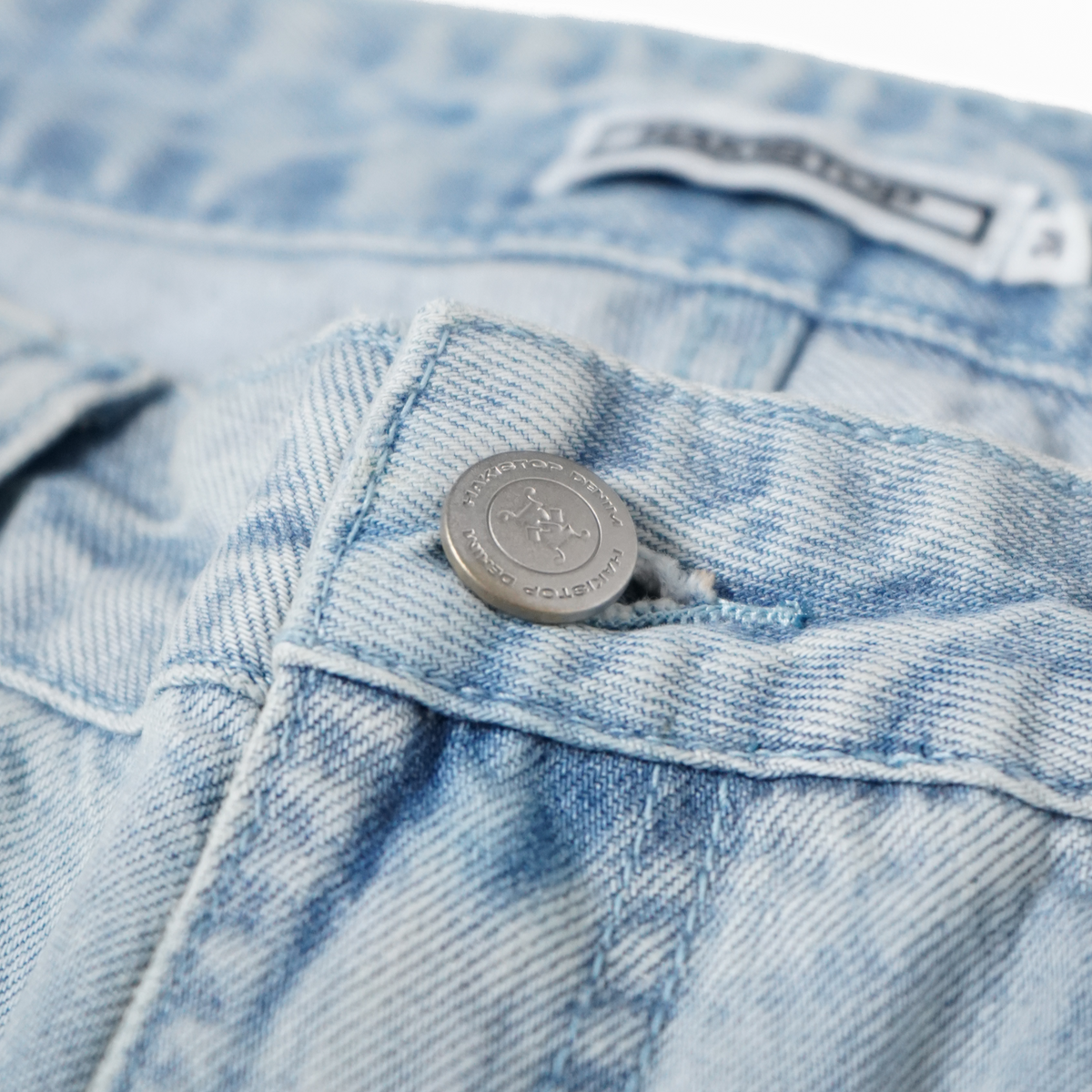 Close-up of a button on a pair of light blue denim jeans with a brand label.